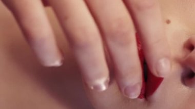 Vertical video. Female protest. Rubbed makeup. Regret disappointment. Unrecognizable sad blonde woman smearing red lipstick on face with hand.