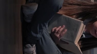 Vertical video. Kid reading hobby. Intelligent child. Night fairy tale. Curious smart cute little girl with open book sitting on floor cross-legged.