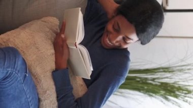 Vertical video. Funny book. Happy woman. Home leisure. Cheerful laughing female reading interesting story light room interior.