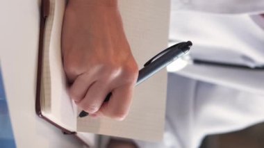 Vertical video. Medical research. Female doctor. Study education. Unrecognizable woman writing information in notebook sitting light room interior.