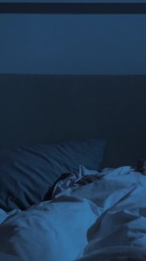Kabus stresi. Gece terörü. Uyku bozukluğu. Kötü bir rüyadan uyanıp karanlık bir yatak odasında uyanan ürkek bir kadın. Dikey video.