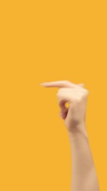Vertical video. Finger pointing. Previous page. Recommending gesture. Female hand sign recommending something before on orange empty space background.