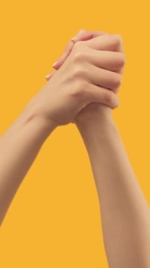 Vertical video. Support gesture. Victory congratulation. Solidarity unity. Female hands showing self-clasping handshake on orange background set of 3 loop.