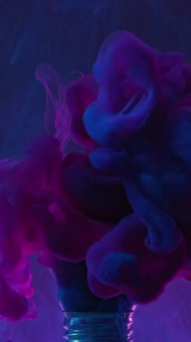 Vertical video. Color fume. Paint splash. Pink blue smoke cloud explosion motion in broken light bulb in water on dark abstract background.