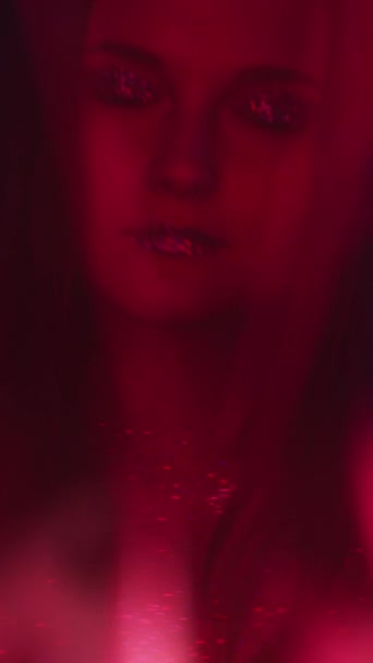 垂直ビデオ カラーライトフェイス ナイトクラブの美しさ ファッションルック ぼかしネオン赤女性とともにキラキラ輝くアートメイクメタリックアイシャドウ唇ダンスオンダーク — ストック動画