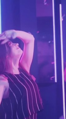 Neon ışıklı kadınlar. Dans partisi. Mutlu kutlamalar. Neşeli bayan arkadaşlar konfeti yağmurunda eğleniyorlar disko mor ışıklarıyla ağır çekimde. Dikey video.