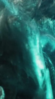 Vertical video. Flower ink. Water paint shot. Underwater explosion. Cyan blue color glowing liquid burst on petals on black background.