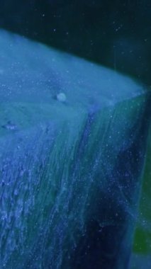 Vertical video. Glitter splash. Ink water. Snow cascade. Blue color paint smoke flow motion over ice cube angle on dark abstract background.