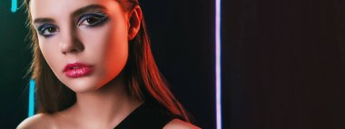 90s look. Fashion makeup. Retro 2000s beauty. Neon light closeup portrait of confident teen girl model face with artistic visage on black copy space background.