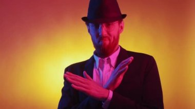 Stop gesture. Protesting man. Neon light portrait. Stylish dissatisfied guy in jacket and hat crossing hands on purple orange background.