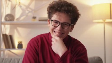 Big money. Rich man. Financial success. Happy smart guy expressing satisfaction holding pile of cash dollars like fan sitting sofa in light room interior.