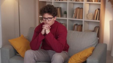 Consider problem. Upset man. Depressed feelings. Calm thoughtful guy sitting sofa in light room interior.