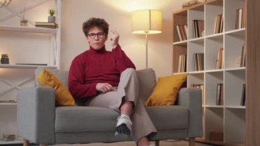 Funny story. Male speaker. Home monolog. Smart happy relaxed man sitting sofa and telling joke in light room interior.