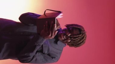 Vertical video. Great idea. Inspired man. Neon light portrait. Happy black guy writing plans in notepad on purple peach pink background.