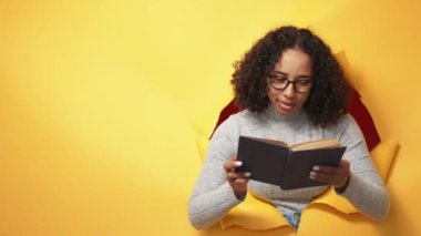 Reading hobby. Learning information. Knowledge education. Curious smart female student with open book in orange breakthrough torn paper hole copy space background.