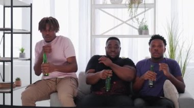 Horror movie. Shocked men. Friendly meeting. Funny scared male friends sitting together with beer and looking TV in light room interior.