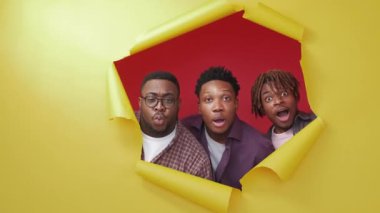 Surprised black men. Wow effect. Shocked expression. Portrait of amazed male friends looking from yellow disrupted paper on red background.