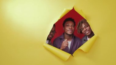 Like sign. Satisfied black men. Great choice. Happy male friends looking from yellow disrupted paper showing supportive gesture on red background copy space.