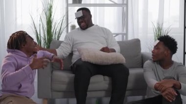 Home entertainment. Black men. Friendly meeting. Inspired hipster guys with papers on forehead playing funny game guess who sitting light room interior.