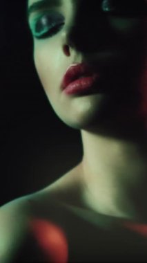 Vertical video. Retro beauty. 90s fashion. Disco night. Closeup of relaxed teen girl model face with artistic makeup closed eyes posing in red green color neon flash light on dark.