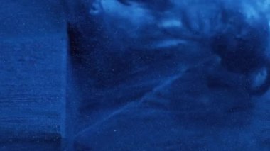 Glitter mist. Paint splash. Fluid wave. Defocused blue color ink wave fume cloud flow motion in water on cube angle on dark abstract background.