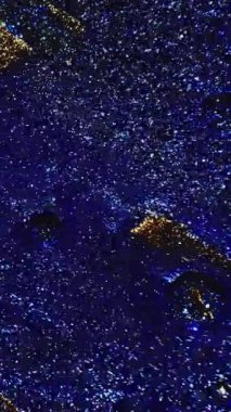 Vertical video. Glitter wave. Paint flow. Sparkling liquid. Defocused shimmering blue golden black color ink mix motion on dark abstract background.