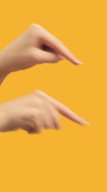 Vertical video. Fingers pointing next. Attention gesture. Female hands recommending something on orange free space advertising background.