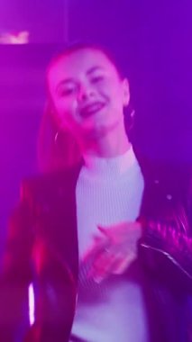 Neon ışıklı kadın. Disko partisi. Kulüp eğlencesi Gece kulübünde mor ışıkta dans eden güzel bir bayan. Dikey video.