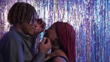 Tender love. Beloved couple. Festive party. Happy black man and woman looking each other touching face embracing on silver cascade curtain background.