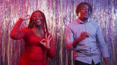 Great party. Happy couple. Holiday celebration. Excited black man and woman having fun showing like gesture on festive cascade curtain background.