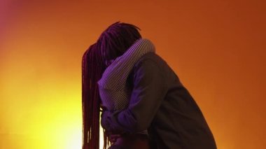 Close relationship. Beloved couple. Neon light portrait. Romantic black man and woman embracing together feeling love on orange purple background.