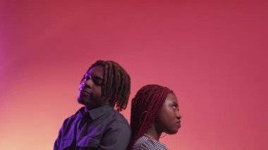Problem relationship. Offended couple. Neon light portrait. Angry black woman and man staying back each other keep silence on purple peach pink background.