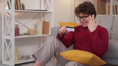 Payment problem. Desperate man. Credit money. Angry nervous guy crying sitting floor looking bank plastic card in light room interior.