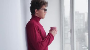 Morning coffee. Considered man. New day inspiration. Calm thoughtful guy with cup hot beverage looking window in light room interior.