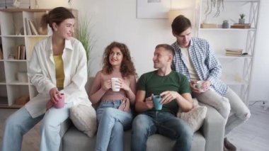 Friendly meeting. Happy people. Enjoying communication. Relaxed hipster guys talking together drinking coffee sitting sofa light room interior.