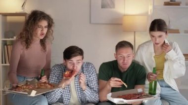 Home TV. Fast food party. Friends meeting. Excited men and women eating pizza drinking beer watching sport competition in light room interior.