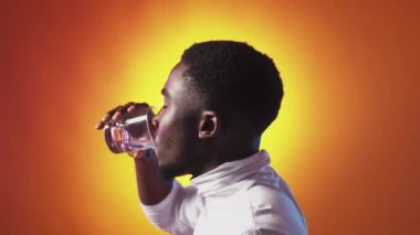 Aqua balance. Water energy. Healthy hydration. Profile of satisfied thirsty man enjoying drinking from glass on orange color gradient copy space background.