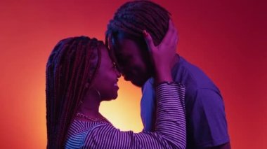 Happy relationship. Beloved couple. Neon light portrait. Close joyful black man and woman embracing together posing on red purple background.