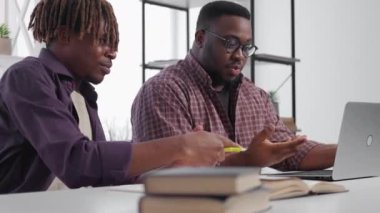 Find decision. Inspired men. Online education. Happy black male students looking satisfied searching in laptop information sitting desk light room interior.