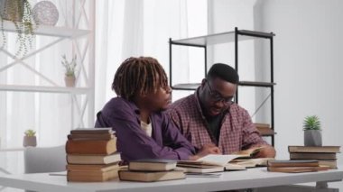 Study together. Male student. Educational process. Inspired black men sitting desk discussing books information in light room interior.