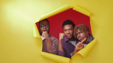Protesting black men. Stop gesture. Bad choice. Strict male friends looking from yellow disrupted paper showing forbidden hands fists up on red background.