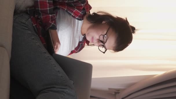 垂直ビデオ 家から仕事だ フリーランスの仕事だ インターネット研究 リビングルームでソファの上にラップトップを使用して入力する眼鏡のリラックスした女性従業員 — ストック動画