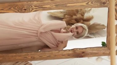 Vertical video. Festive look. Inspired woman. Party preparation. Beautiful middle-aged lady trying on elegant chiffon dress looking mirror in light room interior.