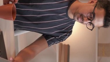 Vertical video. Freelance work. Relaxed man. Online communication. Inspired smiling guy typing laptop drinking coffee sitting desk light room interior.