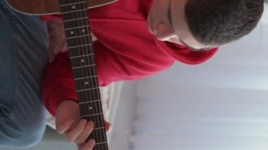 Vertical video. Music practice. Adjusting man. Instrumental hobby. Concentrated guy tuning pegs and gears on string acoustic guitar at home.