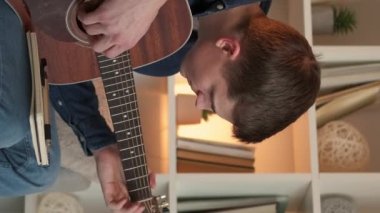 Vertical video. Guitar lesson. Desperate man. Home study. Upset male student struggling to play chords on string instrument sitting couch light room interior.