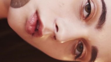 Vertical video. Smooth skin care. Female beauty. Natural look. Pretty woman applying cosmetic brush for compact face powder lens flare blur light.