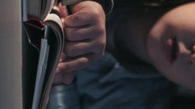 Vertical video. Kid reading hobby. Child education. Imagination development. Closeup of unrecognizable smart little girl studying with open book late at desk.