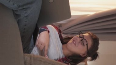 Vertical video. Home web call. Internet communication. Online chat. Relaxed cheerful woman enjoying casual conversation using laptop on cozy couch in living room.