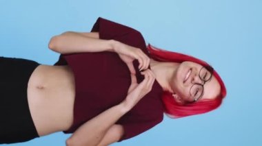 Vertical video. Heart gesture. Love care. Appreciation admiration. Supportive playful girl peeking out showing sympathy hand sign on blue background seamless loop.